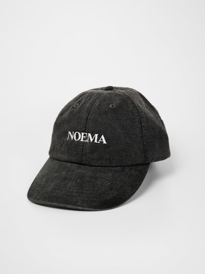 A washed black cotton baseball cap with the brand name 'NOEMA' embroidered in white on the front, photographed on a clean white background.