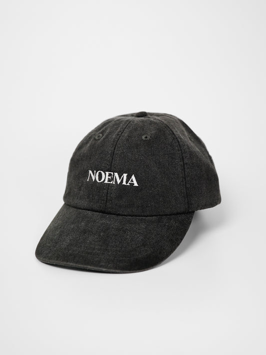 A washed black cotton baseball cap with the brand name 'NOEMA' embroidered in white on the front, photographed on a clean white background.