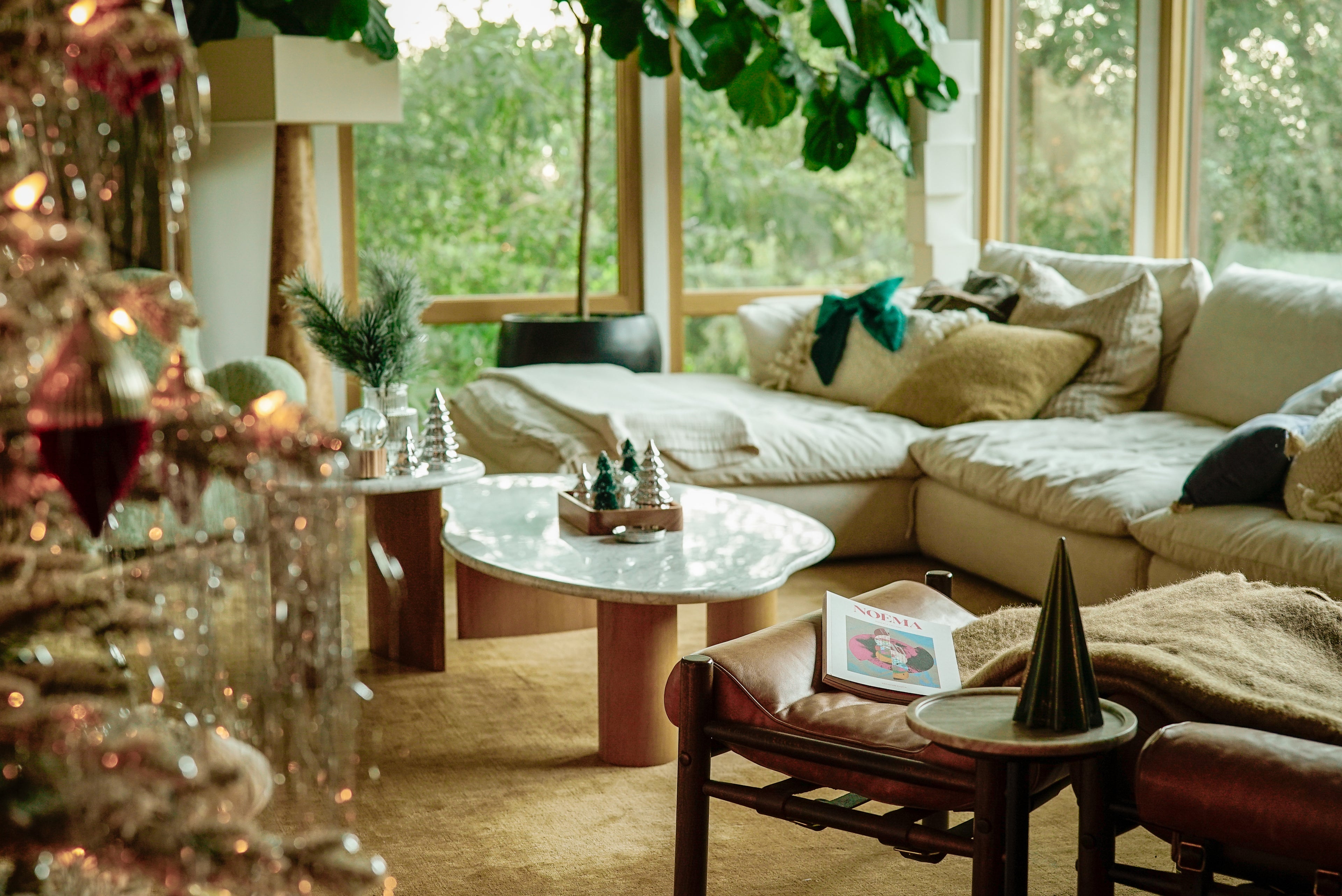 Cozy living room with a Christmas tree, decorations, and a chair showing Noema magazine.